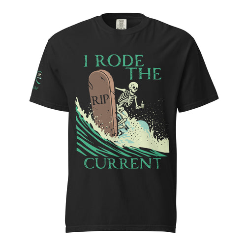 "RIP Current" front print garment-dyed heavyweight tee in black, flat lay showing full skeleton surfing a "RIP" tombstone "I Rode the Current" graphic on front with "17TH & SURF" sleeve emblem – 17th & Surf