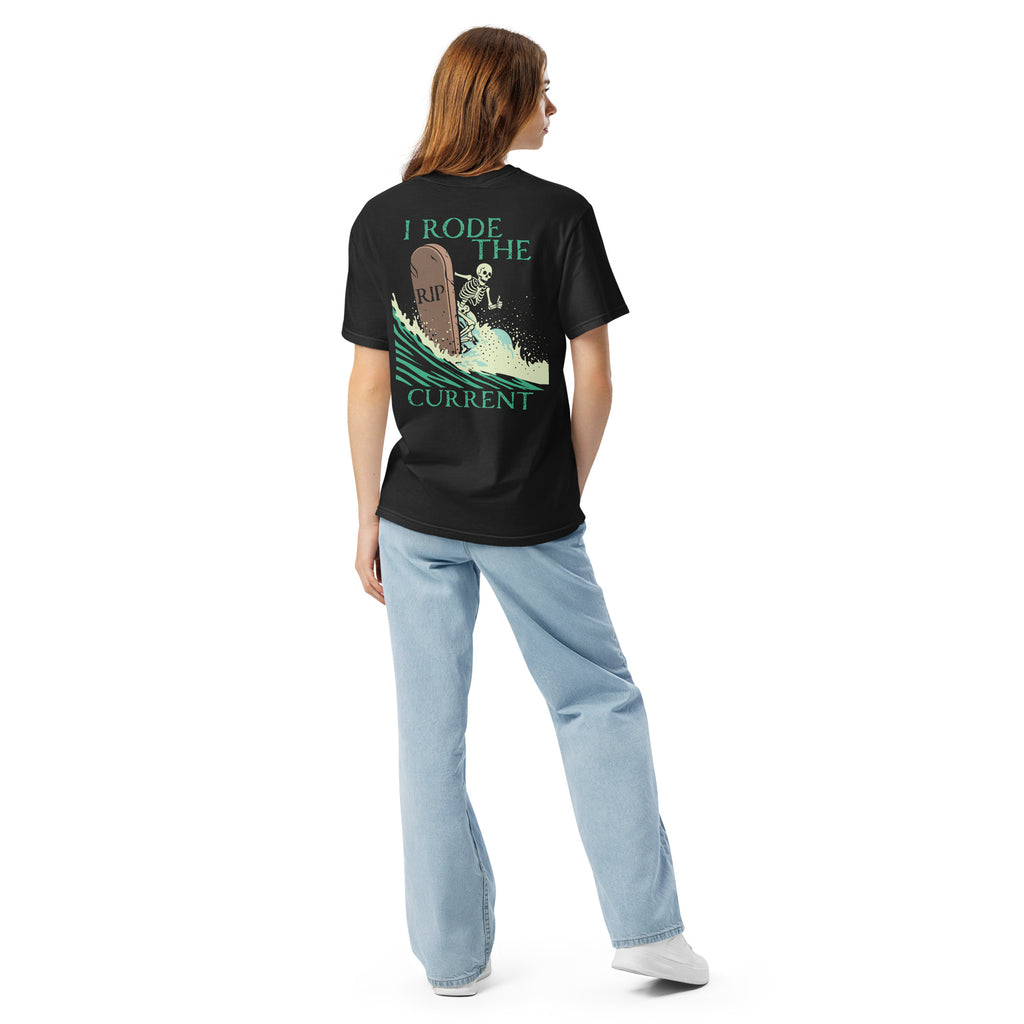 Model wearing "RIP Current" garment-dyed heavyweight tee in black, back view showing skeleton surfing a "RIP" tombstone "I Rode the Current" graphic – 17th & Surf