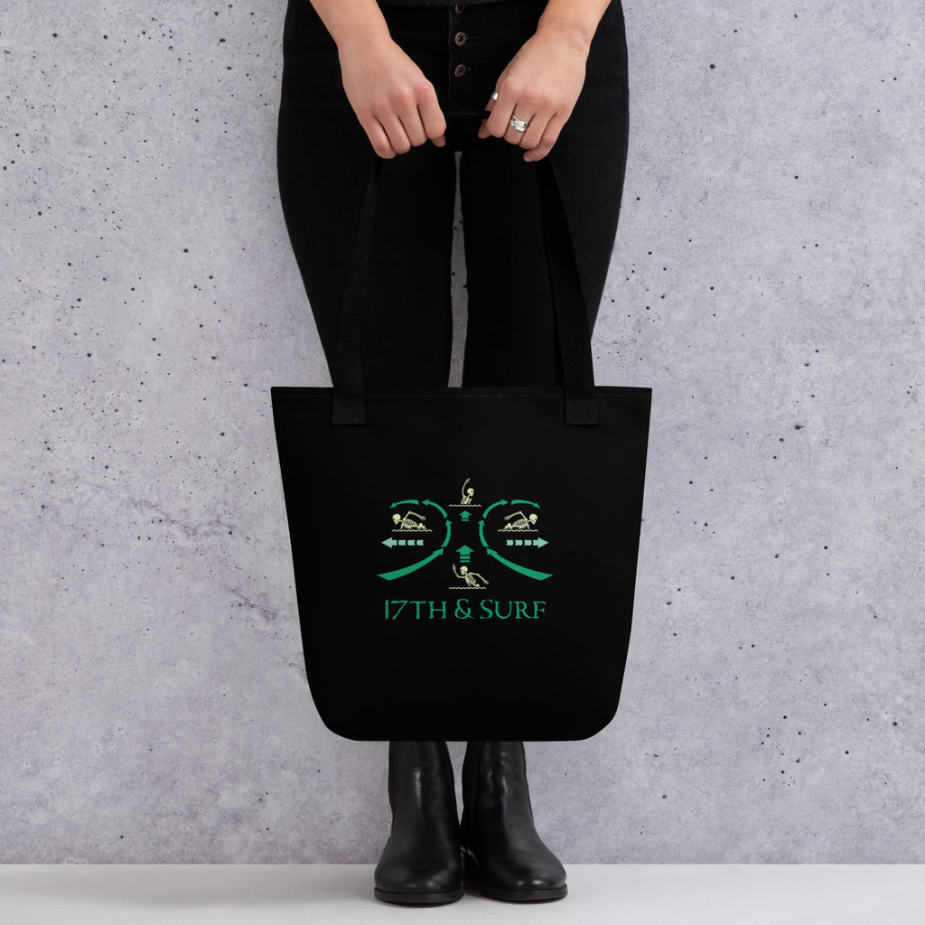 Model holding "RIP Current" all-over print tote bag in black showing reverse side with "17TH & SURF" swimmer emblem – 17th & Surf