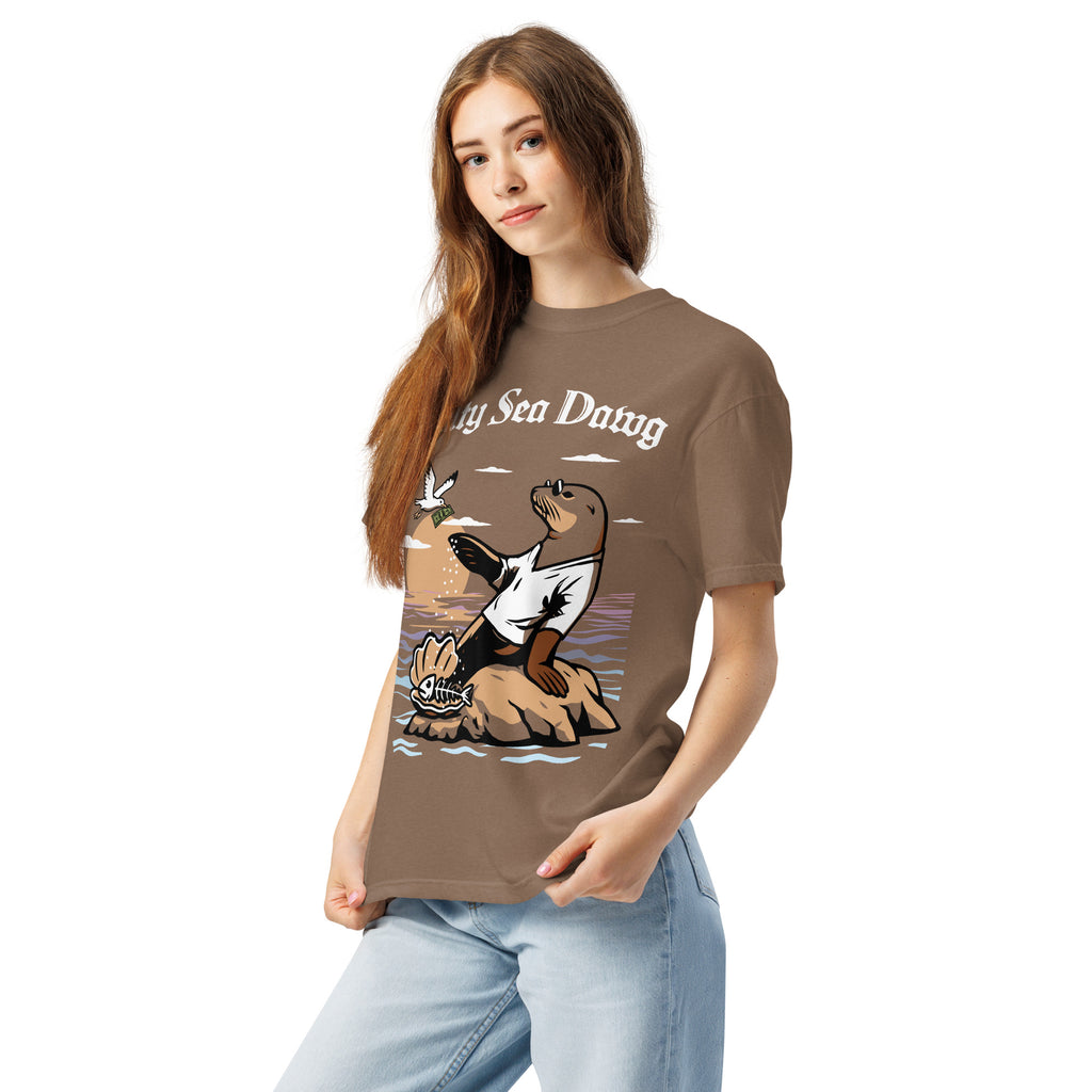 Model wearing "Salty Sea Dawg" front print garment-dyed heavyweight t-shirt in espresso, left front angle view featuring full color graphic of a sea lion sprinkling salt on a clam shell with a fish skeleton beneath arched "Salty Sea Dawg" text – 17th & Surf