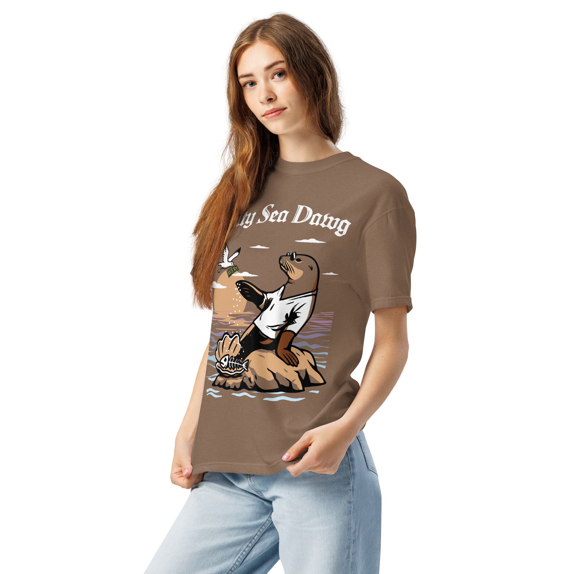 Model wearing "Salty Sea Dawg" front print garment-dyed heavyweight t-shirt in espresso, left front angle view featuring full color graphic of a sea lion sprinkling salt on a clam shell with a fish skeleton beneath arched "Salty Sea Dawg" text – 17th & Surf