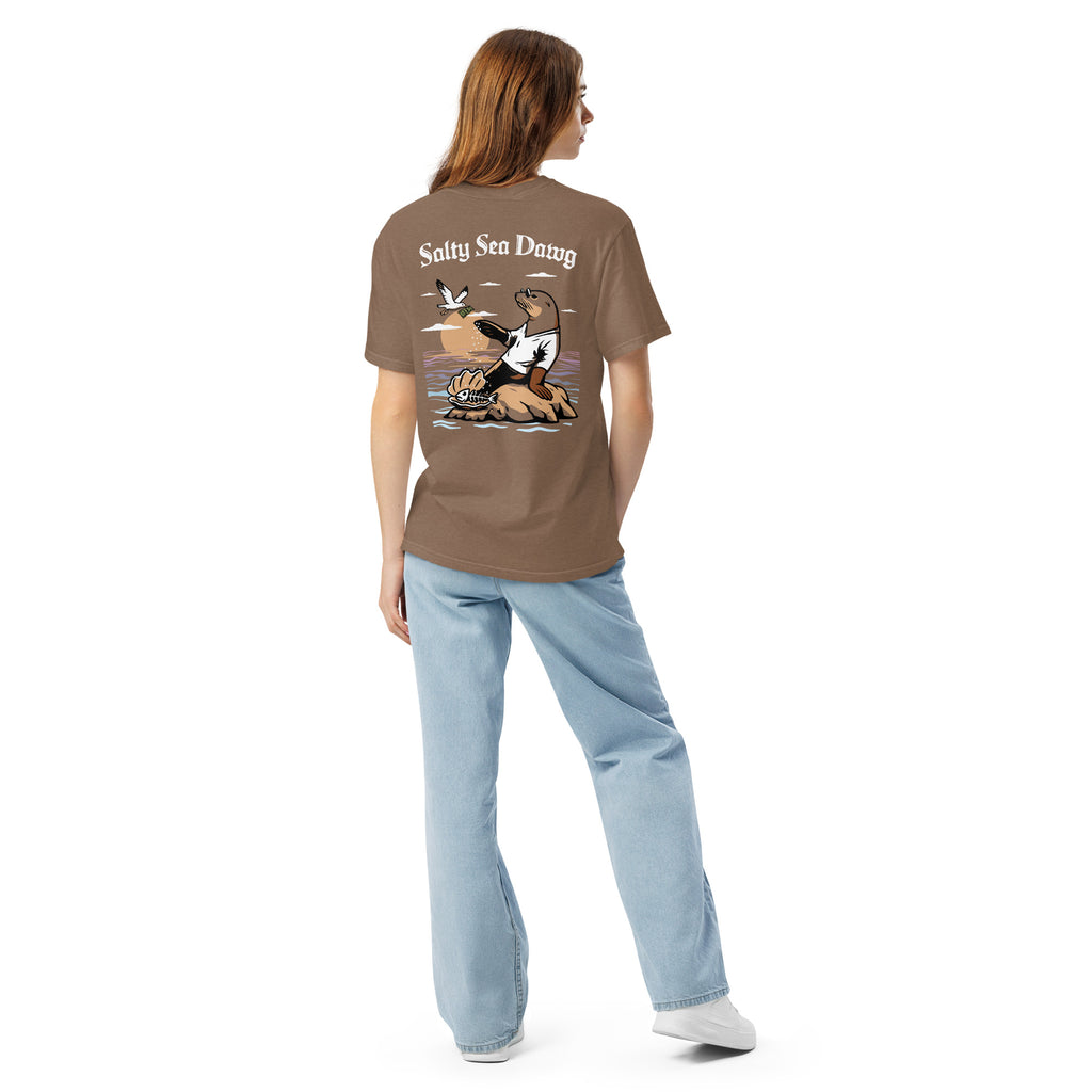 Model wearing "Salty Sea Dawg" garment-dyed heavyweight t-shirt in espresso, back view featuring color graphic of a sea lion sprinkling salt on a clam shell with a fish skeleton beneath arched "Salty Sea Dawg" text – 17th & Surf