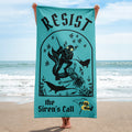 "Resist The Siren's Call" beach towel in teal held up on the beach, featuring black-print arched graphic of a deep-sea diver spearing a mermaid skeleton surrounded by fish and manta rays with "Resist...the Siren's Call" lettering and yellow "17th & Surf" manta ray logo – 17th & Surf