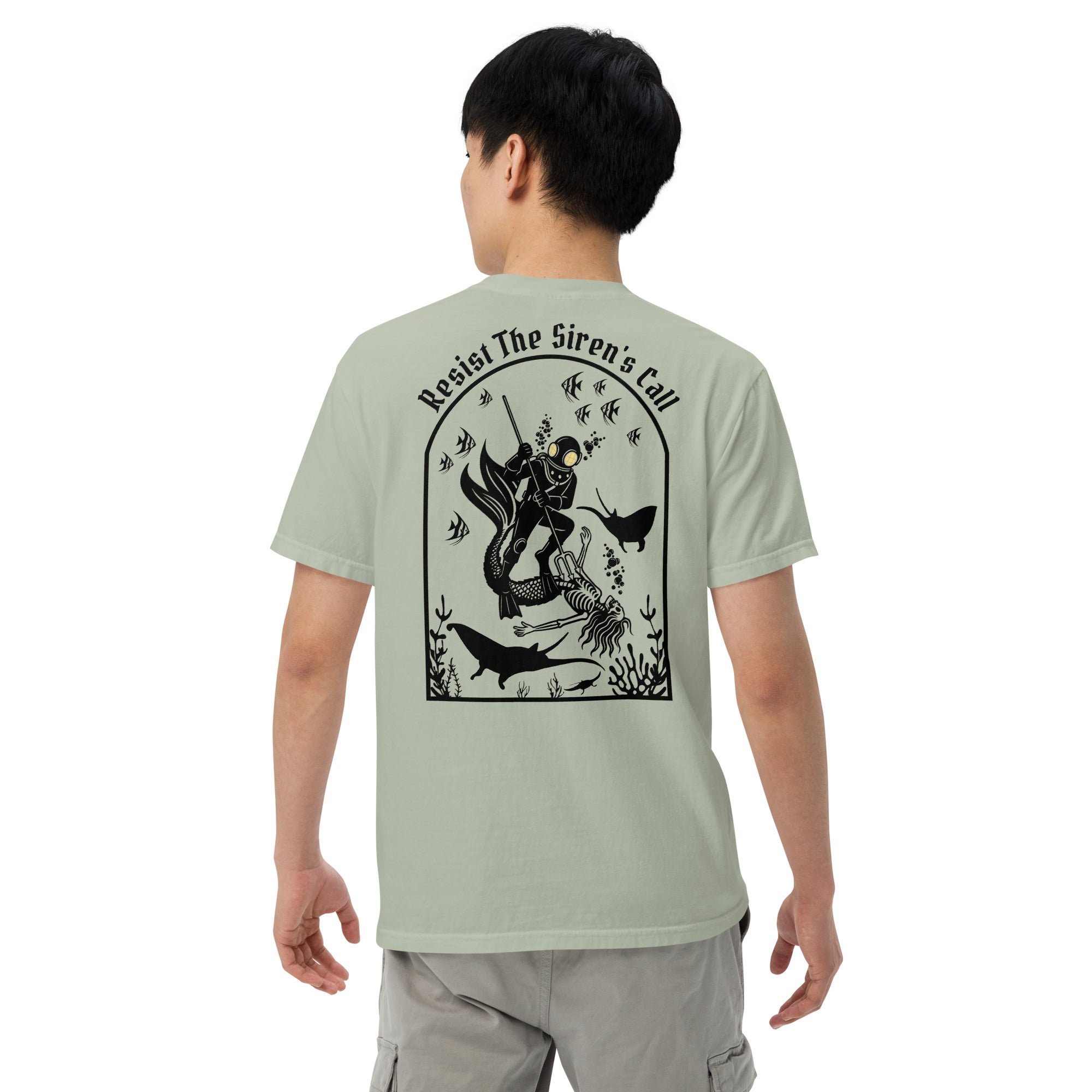 Model wearing "Resist The Siren's Call" black print garment-dyed heavyweight t-shirt in sage bay green, back view featuring black arched graphic of a deep-sea diver spearing a mermaid skeleton surrounded by fish and manta rays – 17th & Surf
