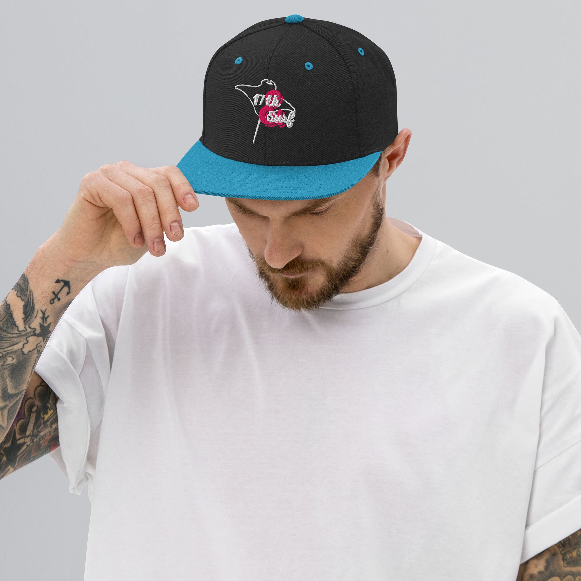 Model wearing the 17th & Surf Stingray snapback hat, black and teal with a white and pink stingray-shaped "17th & Surf" logo – 17th & Surf