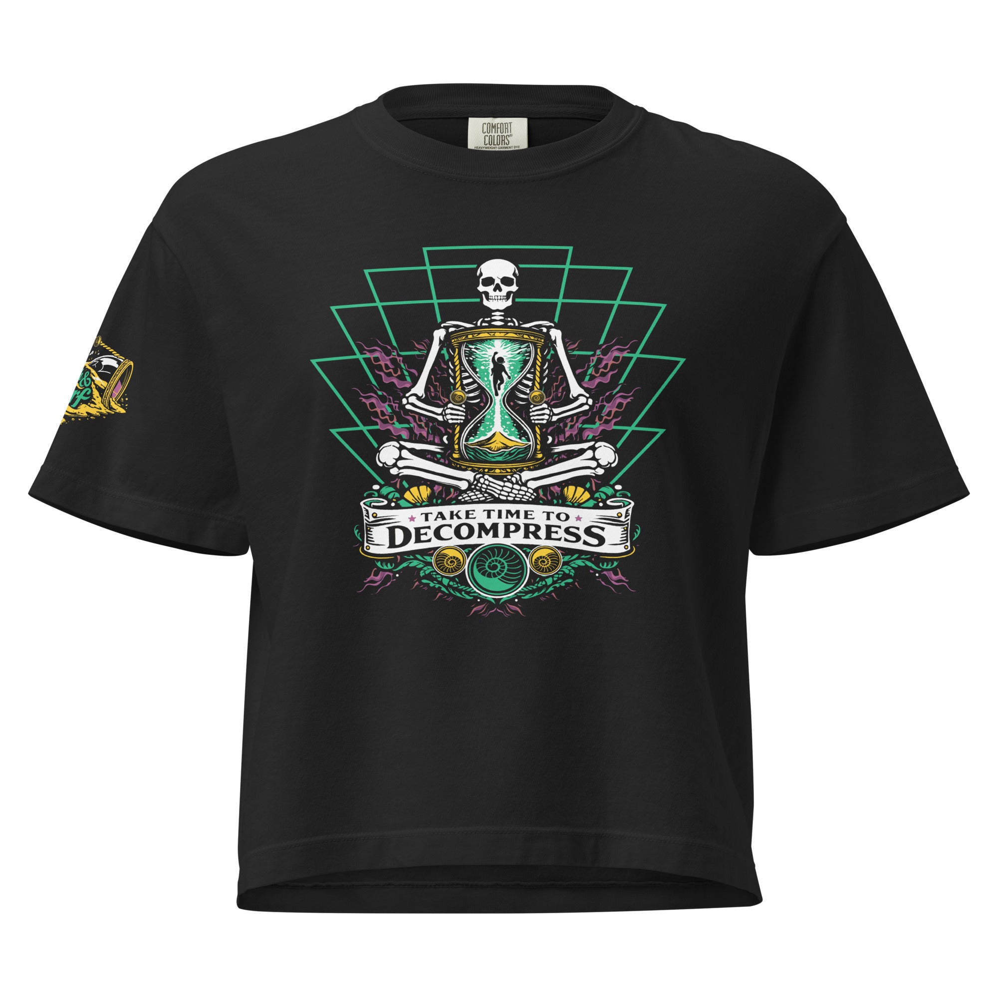 "Take Time To Decompress" black heavyweight boxy t-shirt, front flat lay, featuring a meditating skeleton holding a glowing hourglass with a tiny silhouette inside, framed by a green geometric pyramid pattern with purple coral accents and gold ammonite shells, above a "Take Time To Decompress" banner, with a small gold and teal "17th & Surf" hourglass logo on the sleeve – 17th & Surf