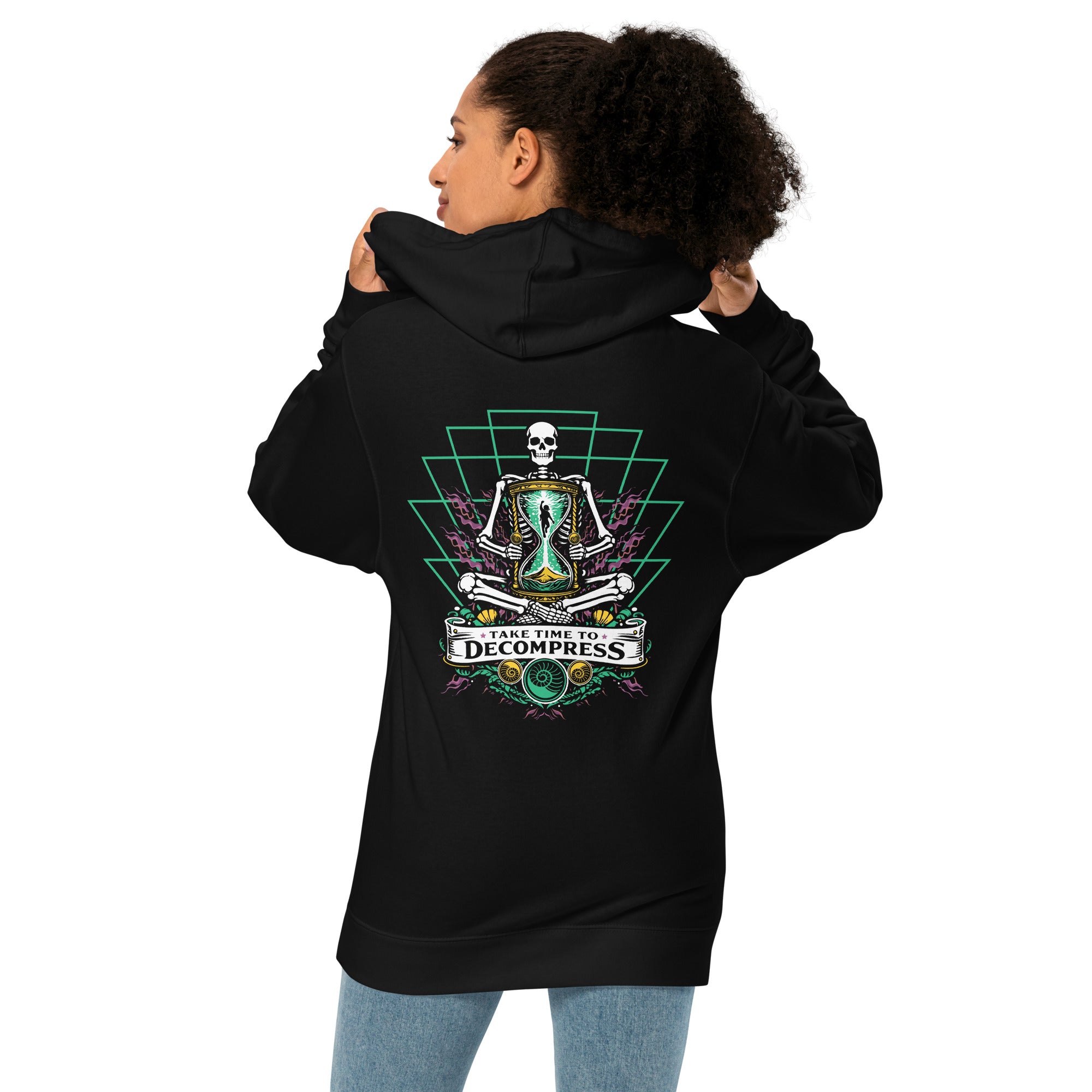 "Take Time To Decompress" black midweight hoodie on female model, back view, featuring a meditating skeleton holding a glowing hourglass with a tiny silhouette inside, framed by a green geometric pyramid pattern with purple coral accents and gold ammonite shells, above a "Take Time To Decompress" banner – 17th & Surf