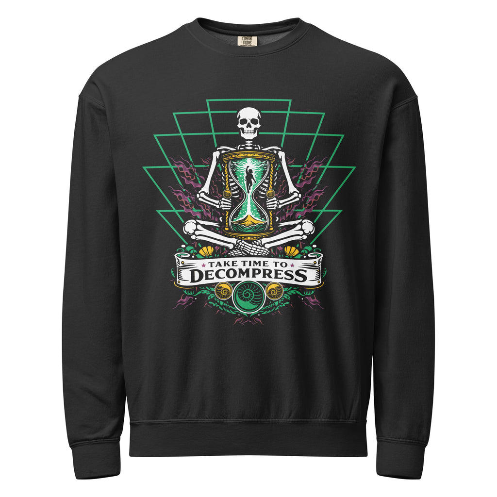 "Take Time To Decompress" black lightweight crewneck sweatshirt, front flat lay, featuring a meditating skeleton holding a glowing hourglass with a tiny silhouette inside, framed by a green geometric pyramid pattern with purple coral accents and gold ammonite shells, above a "Take Time To Decompress" banner – 17th & Surf