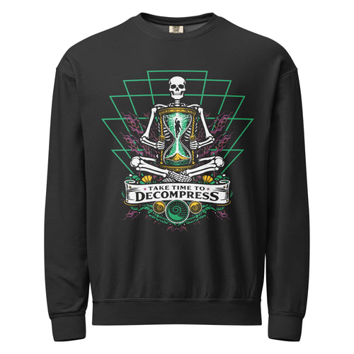 "Take Time To Decompress" black lightweight crewneck sweatshirt, front flat lay, featuring a meditating skeleton holding a glowing hourglass with a tiny silhouette inside, framed by a green geometric pyramid pattern with purple coral accents and gold ammonite shells, above a "Take Time To Decompress" banner – 17th & Surf