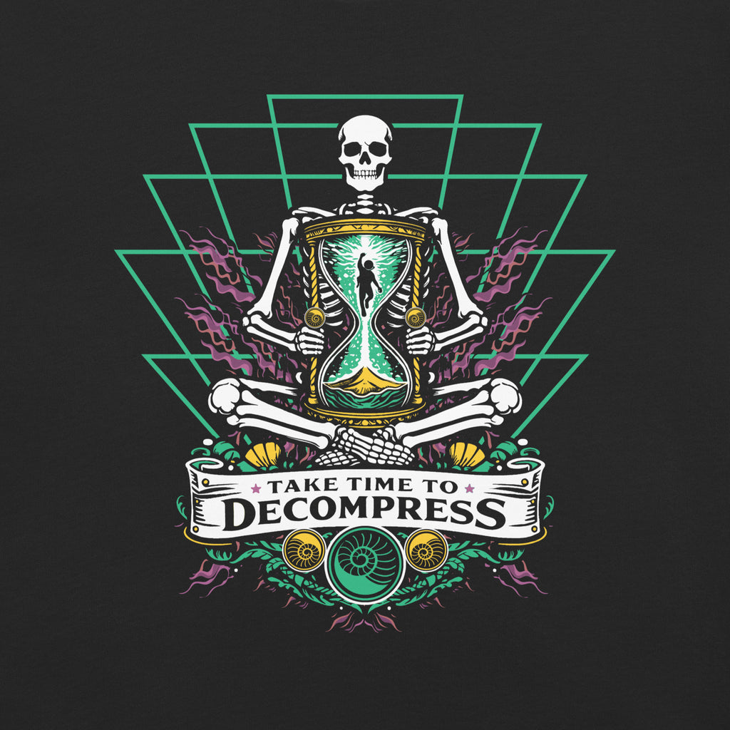 "Take Time To Decompress" black heavyweight t-shirt, close-up back flat lay on dark background, featuring a meditating skeleton holding a glowing hourglass with a tiny silhouette inside, framed by a green geometric pyramid pattern with purple coral accents and gold ammonite shells, above a "Take Time To Decompress" banner – 17th & Surf