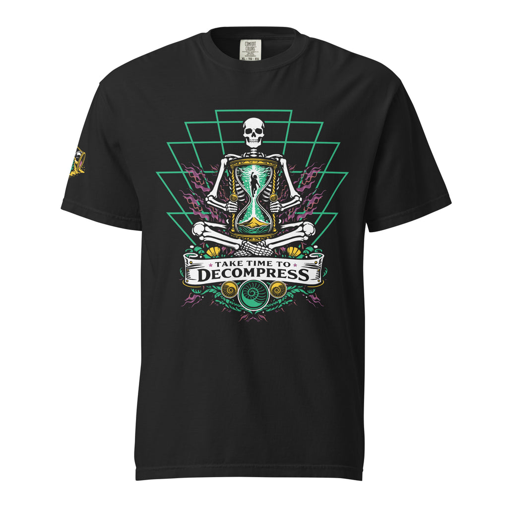"Take Time To Decompress" black heavyweight t-shirt, front flat lay, featuring a meditating skeleton holding a glowing hourglass with a tiny silhouette inside, framed by a green geometric pyramid pattern with purple coral accents and gold ammonite shells, above a "Take Time To Decompress" banner, with a small gold and teal "17th & Surf" hourglass logo on the left sleeve – 17th & Surf