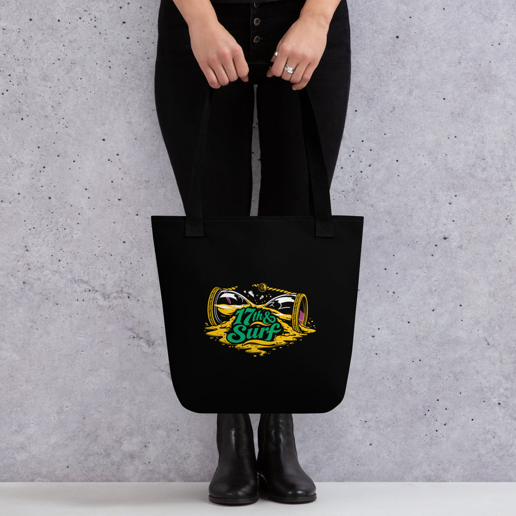"Take Time To Decompress" black tote bag, close-up of the back panel featuring a gold and teal "17th & Surf" hourglass logo – 17th & Surf