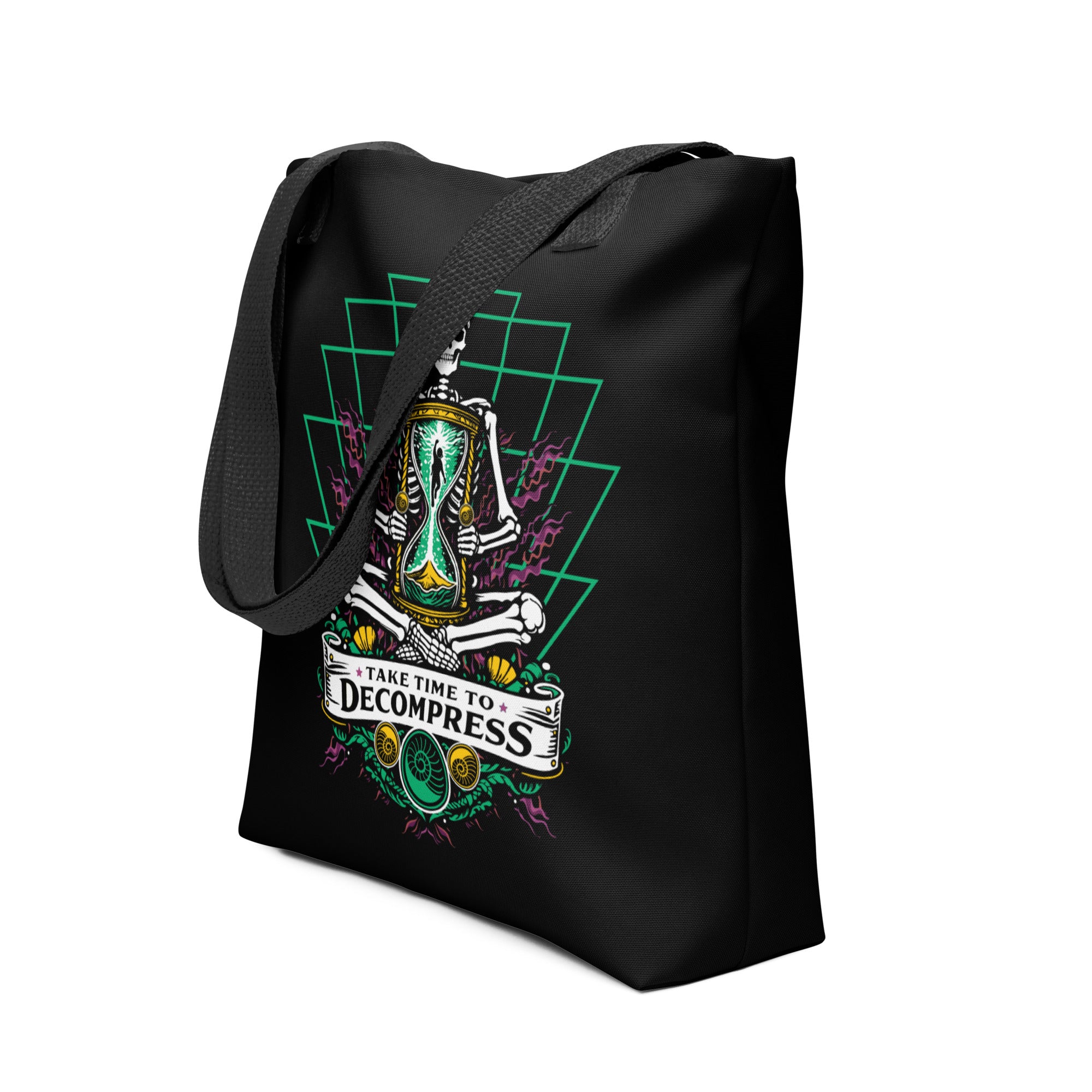 "Take Time To Decompress" black tote bag, 3/4 angle view of the front panel featuring a meditating skeleton holding a glowing hourglass with a tiny silhouette inside, framed by a green geometric pyramid pattern with purple coral accents and gold ammonite shells, above a "Take Time To Decompress" banner – 17th & Surf